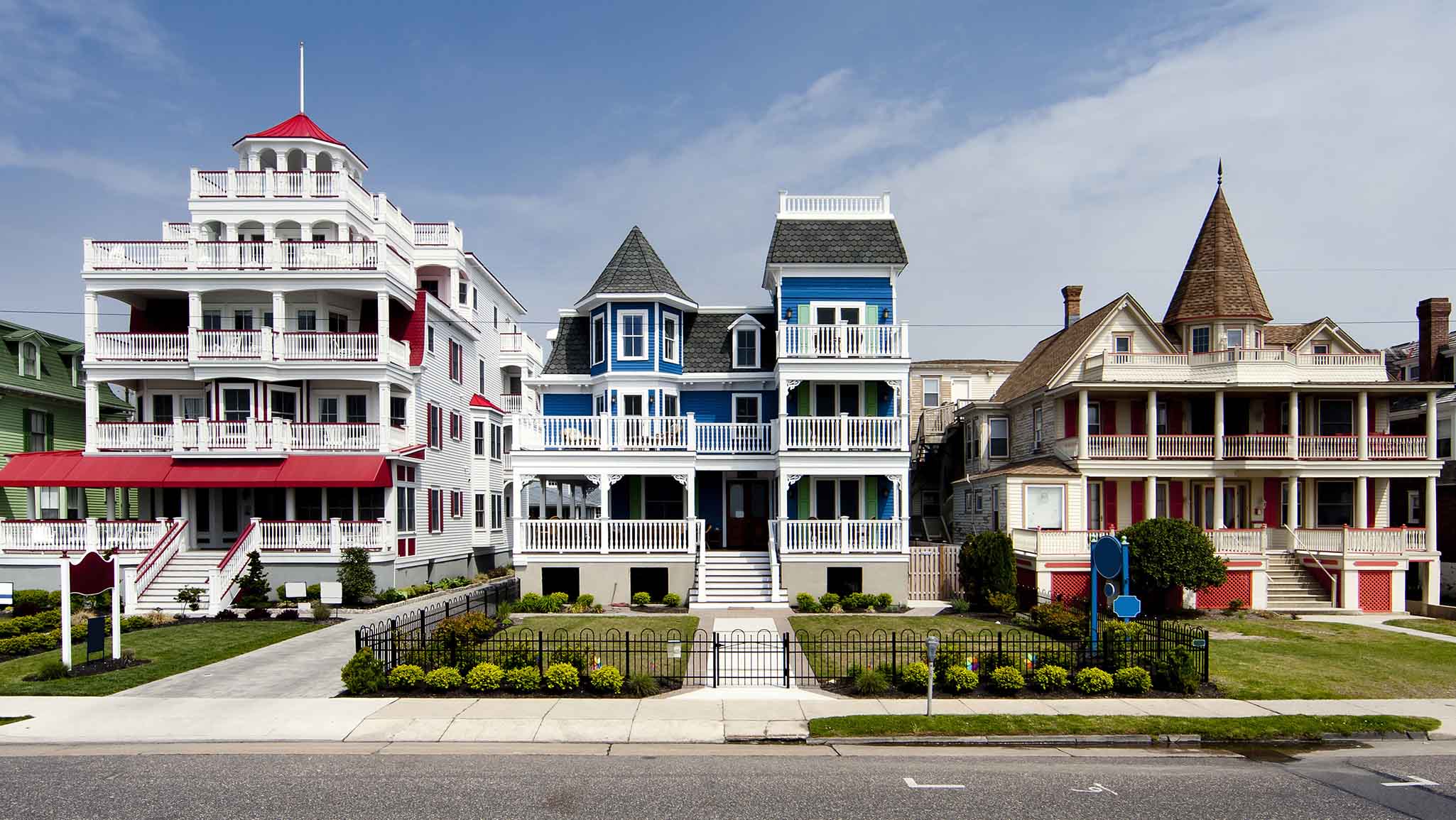 Colorful Victorian style houses alongside a road. Beautiful wooden homes with balconies and porches, painted red, blue, white and orange, under a blue summer spring sky, in Cape May, NJ.